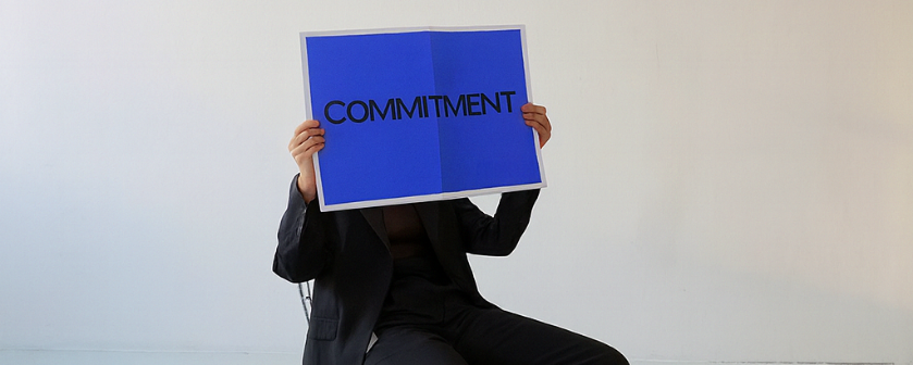 A person holding a blue sign reading commitment